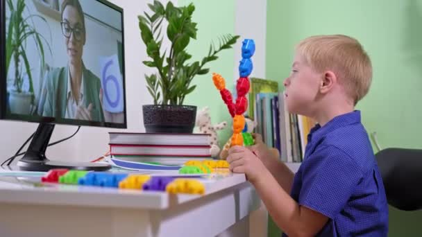 дистанційне навчання під час пандемії, школярка з синдромом Дауна грає з кольоровими іграшками під час навчання з її вчителькою, сидячи вдома з комп'ютером
 - Кадри, відео