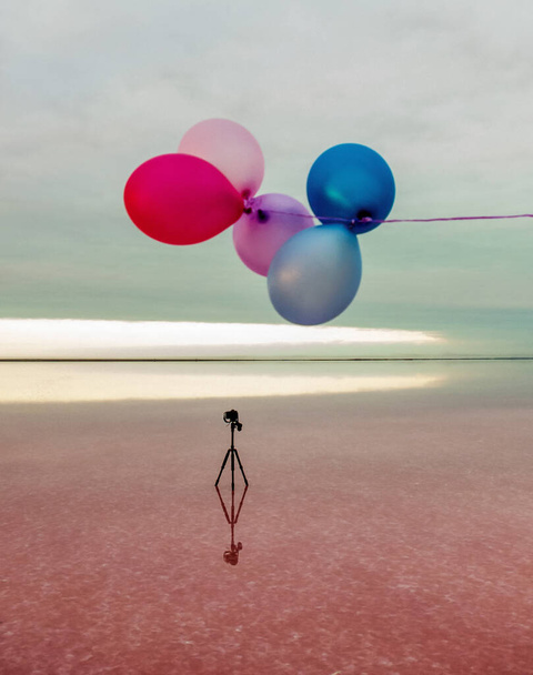 red, blue, pink, blue balloons at sunrise on a pink salt lake and a tripod with a camera - Foto, Imagem