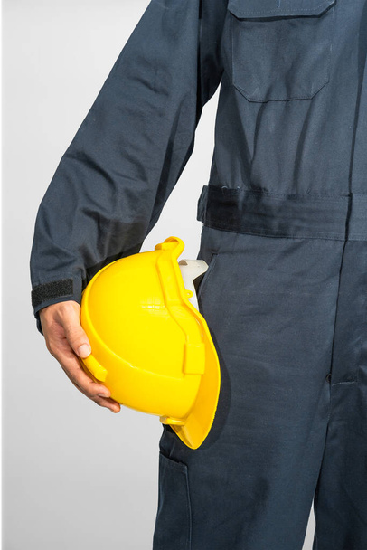 Werknemer in blauwe overall met gele hardhoed geïsoleerd op grijze achtergrond - Foto, afbeelding