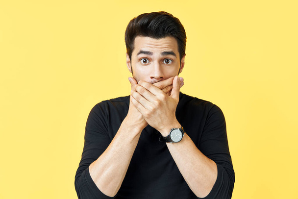 Shocked man covering mouth with hands over yellow background. - Foto, imagen