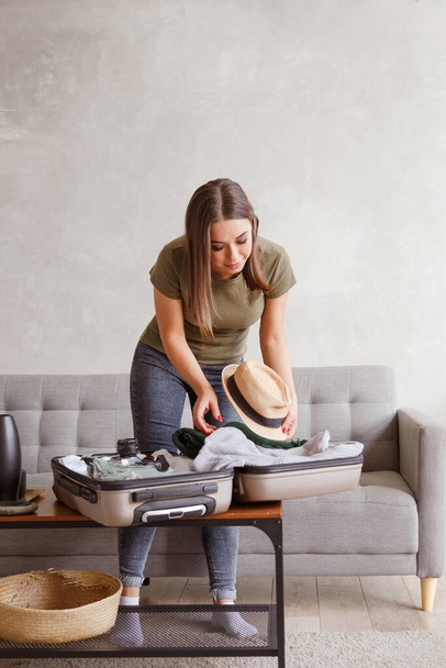 Suitcase preparation for a vacation trip after lock down. Young woman checking clothes and stuff in luggage on the sofa at home before travel - 写真・画像