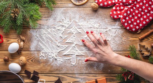 The Christmas tree is drawn on flour, which is scattered on a wooden table. Concept of New Year's mood and preparation of festive pastries. - Foto, Imagen