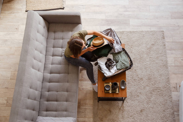 Suitcase preparation for a vacation trip after lock down. Young woman checking clothes and stuff in luggage on the sofa at home before travel - Foto, Imagen