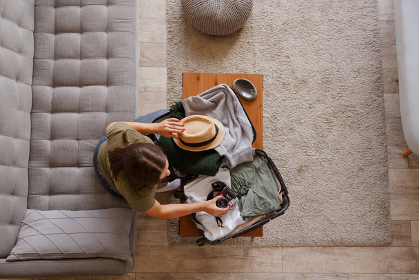 Подготовка чехла для отпуска после закрытия. Молодая женщина проверяет одежду и вещи в багаже на диване дома перед поездкой - Фото, изображение