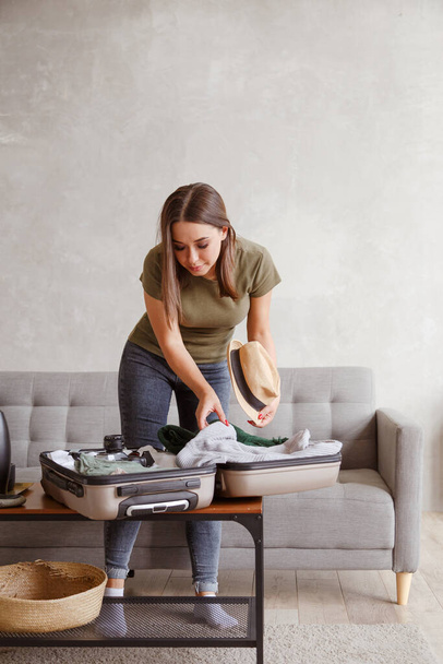 Подготовка чехла для отпуска после закрытия. Молодая женщина проверяет одежду и вещи в багаже на диване дома перед поездкой - Фото, изображение