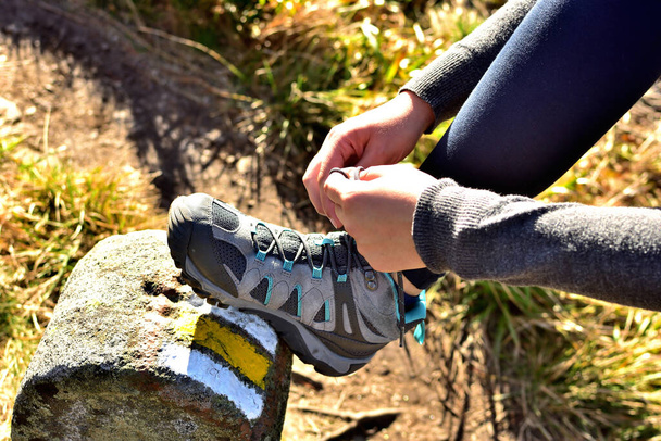 Close-up of hiker tying her trekking shoes on a hiking stone marking the tourist route - Photo, Image