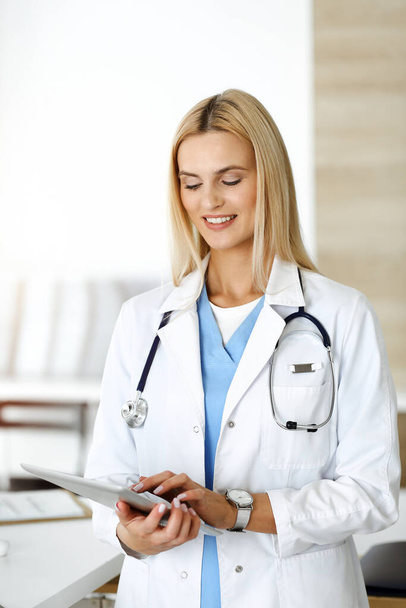 Woman-doctor controls medication history records and exam results while using tablet computer in sunny hospital. Medicine and healthcare concept - Photo, image