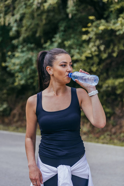 Жінка-спортсменка п'є воду, освіжає, зволожує після тривалого тренування, біжить
. - Фото, зображення