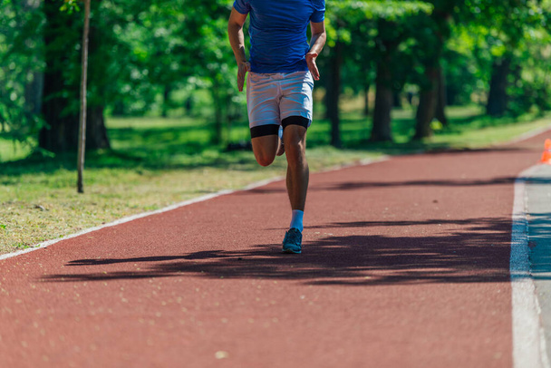 Foto van hardloopschoenen en sterke atletische benen van sportman joggen op de hardloopbaan - Foto, afbeelding
