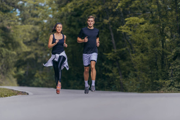 Athletic couple running on a street next to each other. Nature,fit and healthy concept. - Photo, Image