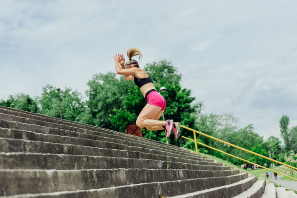 Ajuste atleta sano, mujer hermosa en ropa deportiva apretada saltando en las escaleras, calentando antes de trotar mientras que mira altamente motivado. - Foto, imagen