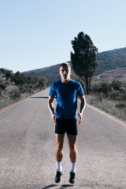 Ajuste atleta masculino corriendo en un camino abierto en el bosque en un escenario post-apocalíptico. - Foto, imagen