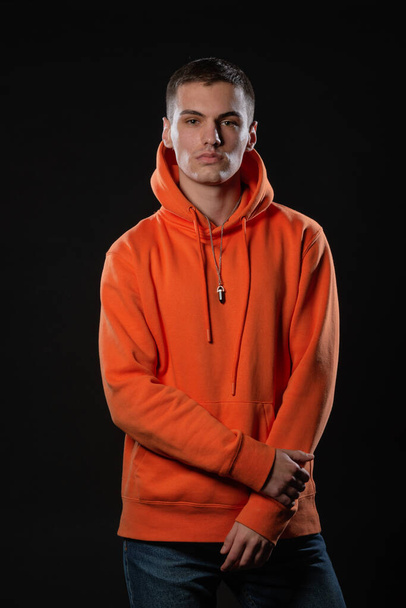 close-up portret van een knappe man model op zoek serieus terwijl poseren in oranje hoodie in een studio - Foto, afbeelding