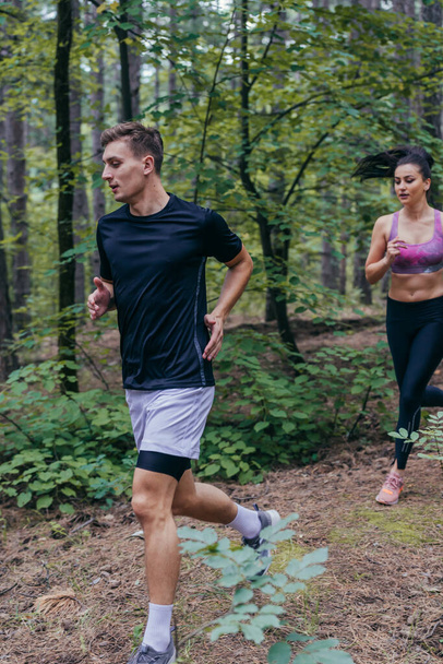 Young athletic couple is running outdoors in the wooded forest area - Photo, Image