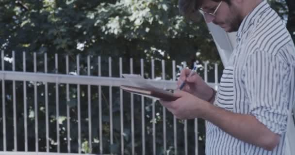 Biznesmen pracujący zdalnie, zapisujący swoje myśli na kartce papieru - Materiał filmowy, wideo