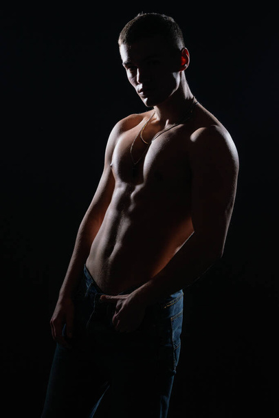 Retrato de silueta de alto contraste de un sexy modelo masculino joven sin camisa posando en el lado. - Foto, imagen