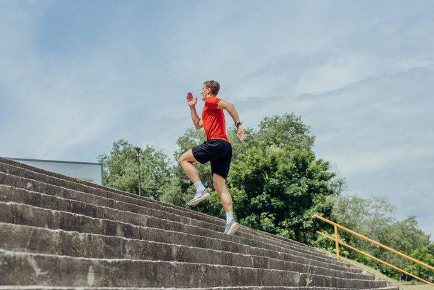 Genç ve çekici erkek sporcu parkta merdivenlerde koşuyor ve egzersiz yapıyor.. - Fotoğraf, Görsel