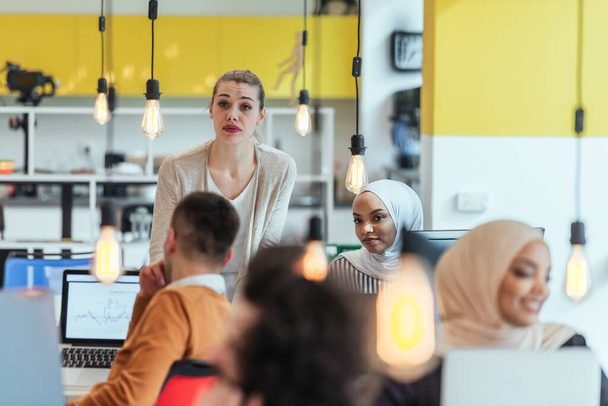 Groep collega 's, teamgenoten helpen hun nieuwe Afro-Amerikaanse, zwarte, moslim collega hijab dragen om te integreren in het moderne bedrijf. Multi-etnische collega 's in een modern startup bedrijf. - Foto, afbeelding
