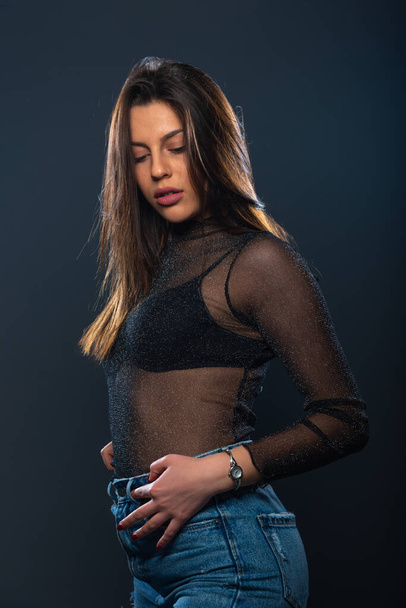 Sensual portrait of an attractive female model posing in jeans and sparkling transparent shirt - Photo, Image