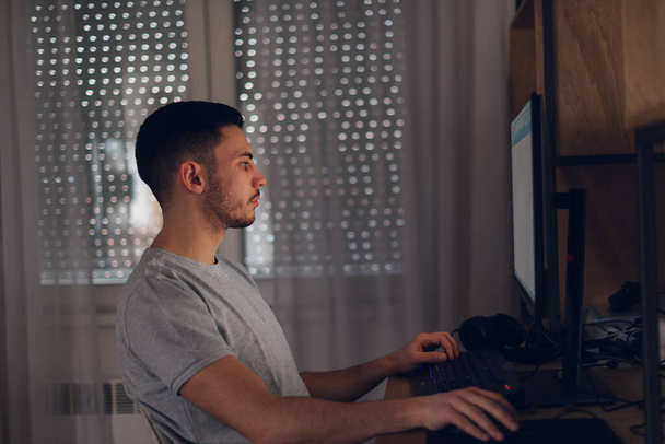 Programmeur werkt op zijn computer terwijl het schermlicht weerkaatst op zijn gezicht. - Foto, afbeelding
