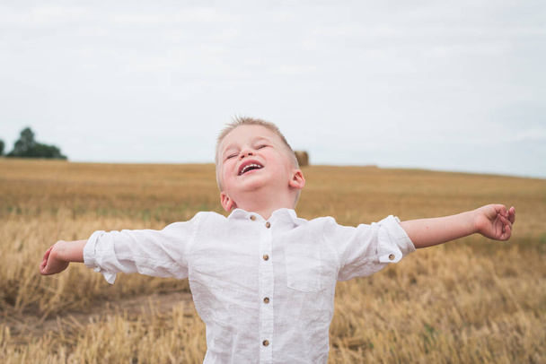 Handsome little boy in white shirt is photographed in a wheat field - Fotoğraf, Görsel