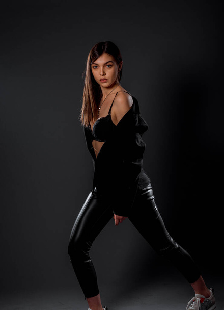 Studio body shot van een trendy jonge vrouw in moderne stijl jacketshirt en latex broek - Foto, afbeelding