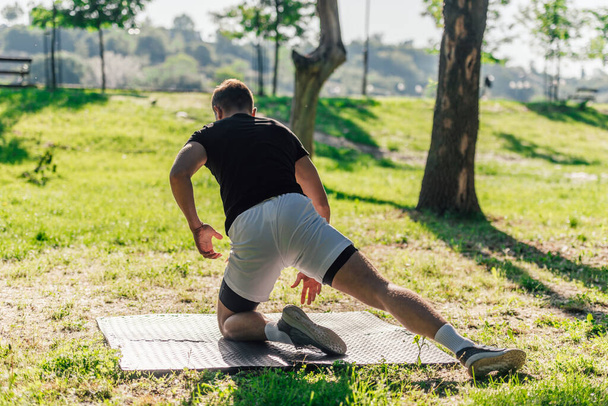 Υγιής νεαρός άνδρας κάνει εξωτερική προθέρμανση ασκήσεις τεντώματος σε ένα στρώμα γυμναστικής - Φωτογραφία, εικόνα