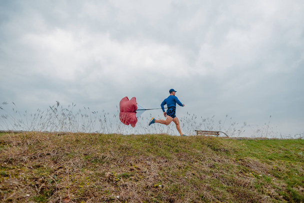 Hombre mayor bien construido en ropa deportiva corriendo con un paracaídas de velocidad - Foto, Imagen