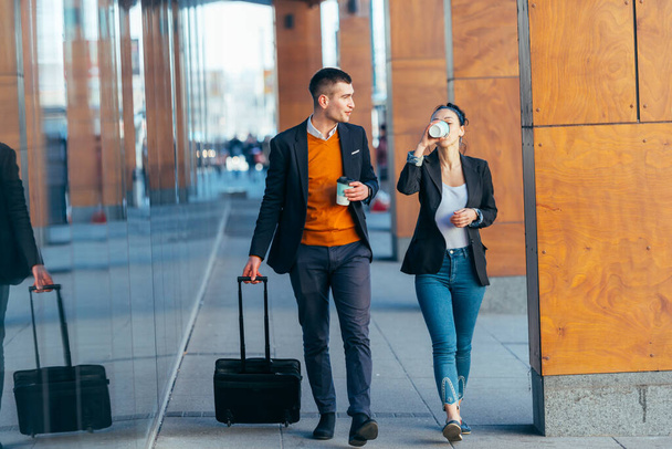 Деловая пара (коллеги) прогуливаясь по футуристическому современному вокзалу (аэропорту), выпивая кофе и разговаривая друг с другом. - Фото, изображение