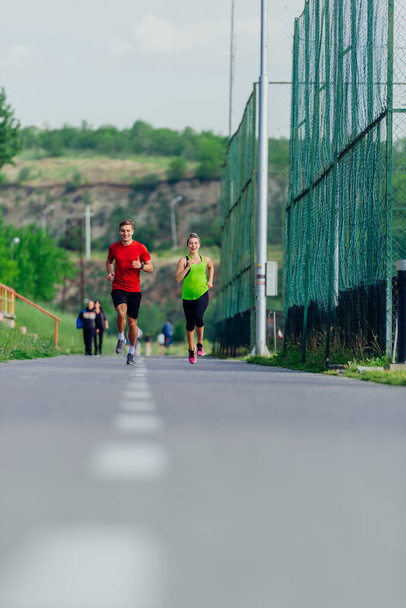 Молодые спортсмены и спортсменки бегают и бегают по дороге в парке - Фото, изображение
