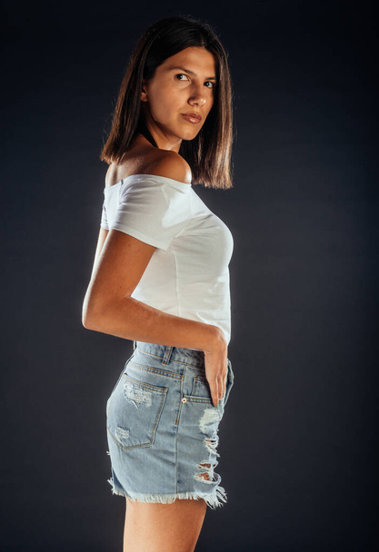 Portrait of an attractive woman posing in white top and ripped short jeans - Photo, Image
