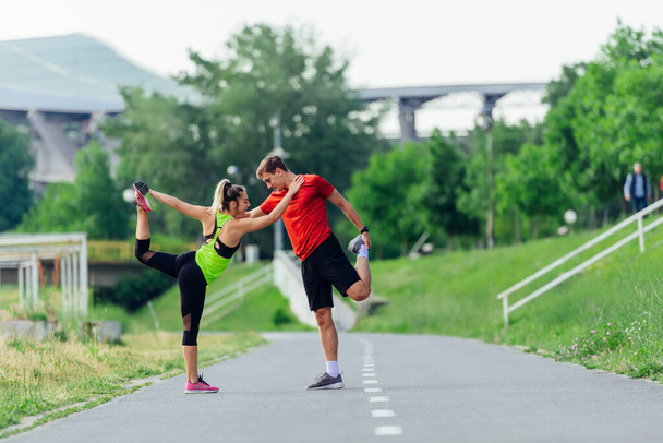 Young couple  warming up and stretching together in a park before running - Φωτογραφία, εικόνα