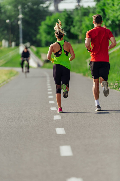 Vista desde la parte posterior de una joven pareja deportiva corriendo en el parque - Foto, Imagen