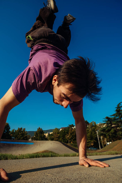 Физически сильный мужчина держит свое тело на руках в скейтпарке
 - Фото, изображение