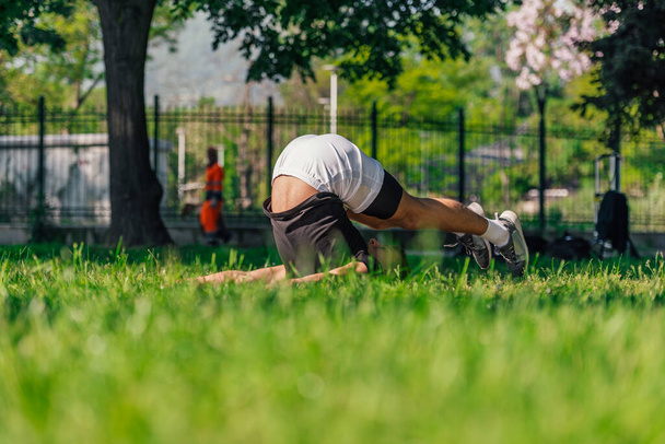 młody sportowy przystojny mężczyzna praktykuje jogę w parku i robi pług poza. - Zdjęcie, obraz