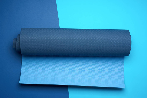 tapete de neoprene azul torcido encontra-se em um fundo azul, equipamentos esportivos, vista superior - Foto, Imagem