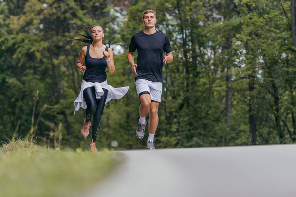 Young fit couple atheltes running on running road in a forest. - Photo, Image