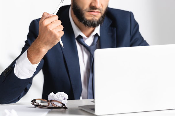 Cropped view of stressed businessman holding broken pencil near eyeglasses, laptop and clumped paper in office  - Photo, Image
