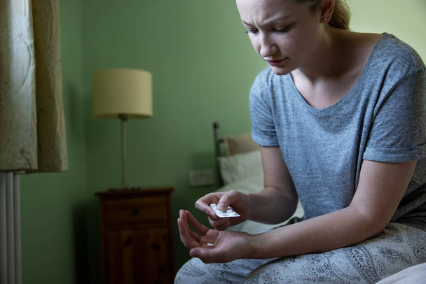 Woman Sitting On Bed Wearing Pyjamas Taking Medication - Foto, immagini