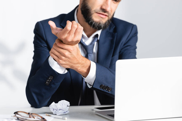 Обрізаний вид бізнесмена відчуває біль в руці біля гаджетів і забитий папір на столі
  - Фото, зображення