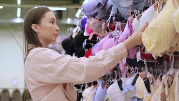 młoda kobieta kupuje biustonosz w sklepie z bielizną - Materiał filmowy, wideo