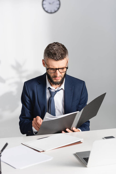 Businessman holding paper folder near gadgets on blurred foreground in office  - Foto, Bild