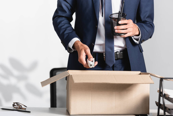 Обрезанный вид уволенного бизнесмена с канцелярскими принадлежностями возле коробки на столе в офисе  - Фото, изображение
