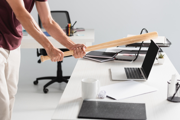 Cropped view of businessman beating laptop with baseball bat near paper folder on blurred foreground  - Photo, Image