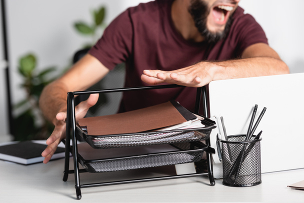 Oříznutý pohled na křičící podnikatel házení papírnictví a notebook ze stolu  - Fotografie, Obrázek