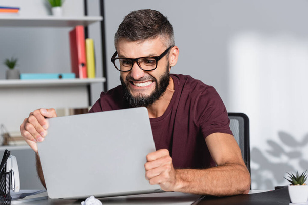 Boze zakenman met laptop tijdens zenuwinzinking op kantoor  - Foto, afbeelding