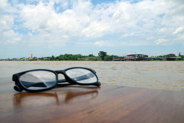 Chaophraya川の美しい景色と焦点を前に、ガラスの木製のテーブルの上に配置され、青い空に多くの白い雲. - 写真・画像