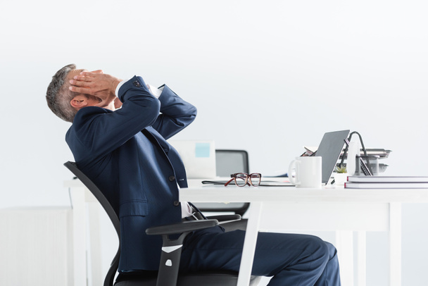Hombre de negocios cansado tocando la cara cerca de la computadora portátil y anteojos en primer plano borrosa en la oficina   - Foto, Imagen