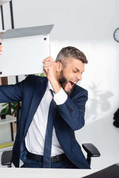Gritando empresario sosteniendo portátil durante la crisis nerviosa en la oficina  - Foto, Imagen