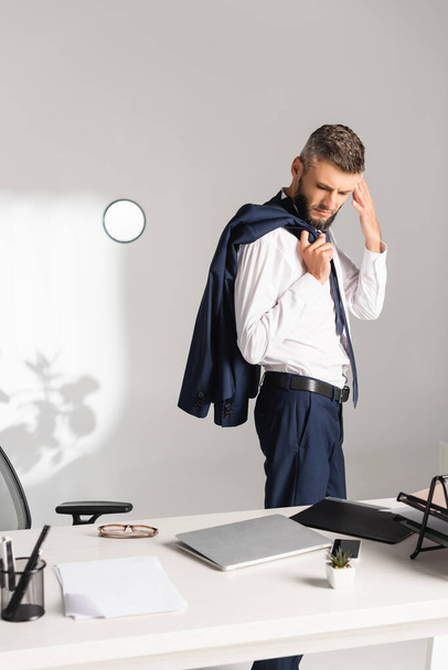 Businessman holding jacket near gadgets and paper folder on working table  - Фото, зображення